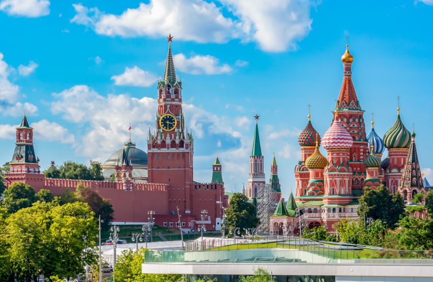 View of the Kremlin and St. Basil's Cathedral in Moscow, Russia, under a bright blue sky, showcasing the city's famous architectural landmarks.